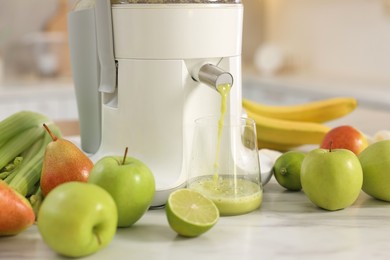 Photo of Modern juicer, fruits and glass on white marble table, closeup