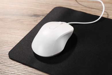 Photo of Computer mouse with mousepad on wooden table, closeup