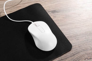 Photo of Computer mouse with mousepad on wooden table, closeup. Space for text