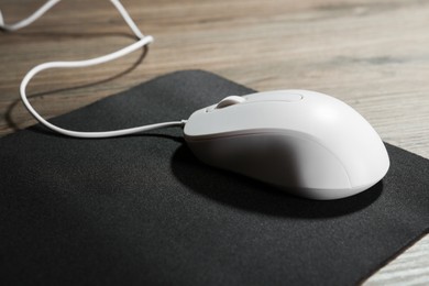 Photo of Computer mouse with mousepad on wooden table, closeup