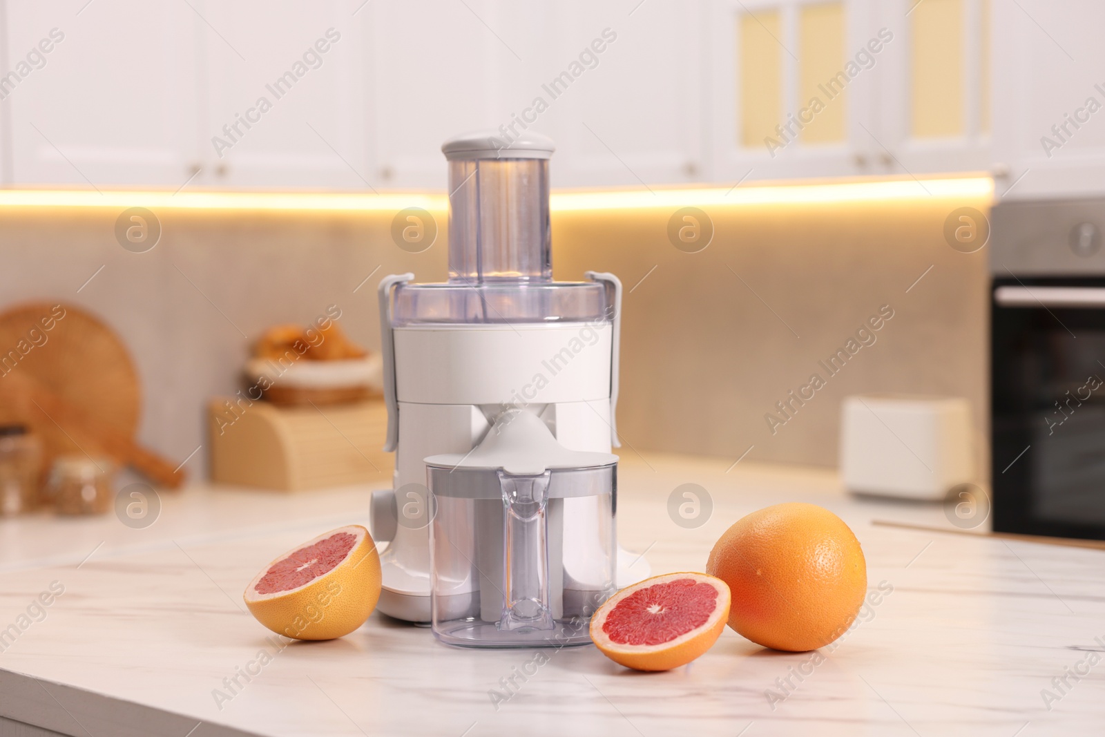 Photo of Modern juicer and fresh grapefruits on white marble table in kitchen