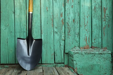 Photo of Metal shovel near turquoise wooden wall. Gardening tool