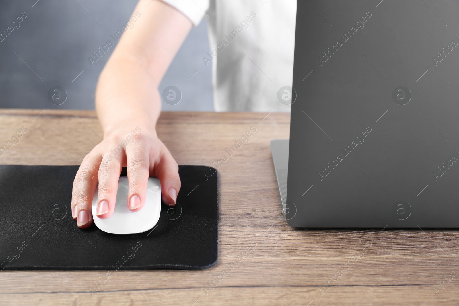 Photo of Woman using computer mouse while working with laptop at wooden table, closeup