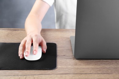 Photo of Woman using computer mouse while working with laptop at wooden table, closeup