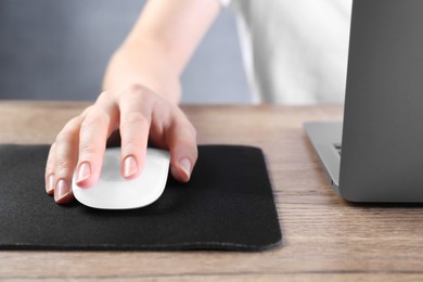 Photo of Woman using computer mouse while working with laptop at wooden table, closeup