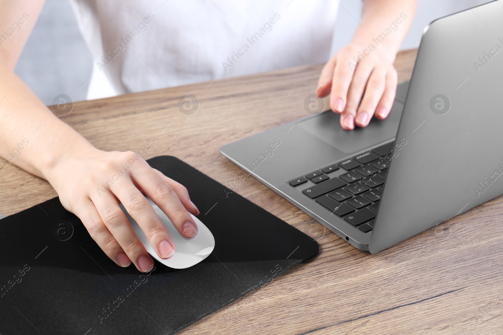 Photo of Woman using computer mouse while working with laptop at wooden table, closeup