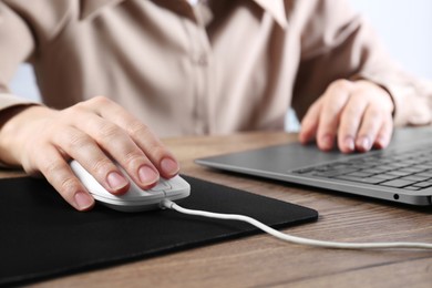 Photo of Woman using computer mouse while working with laptop at wooden table, closeup