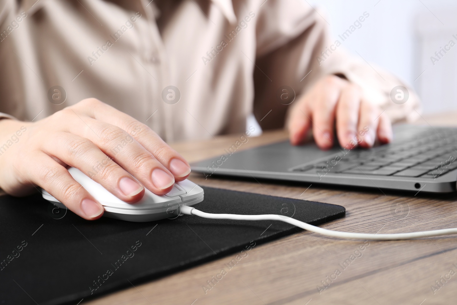 Photo of Woman using computer mouse while working with laptop at wooden table, closeup