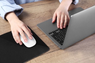 Photo of Woman using computer mouse while working with laptop at wooden table, closeup