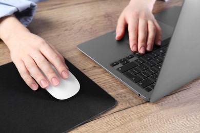 Photo of Woman using computer mouse while working with laptop at wooden table, closeup