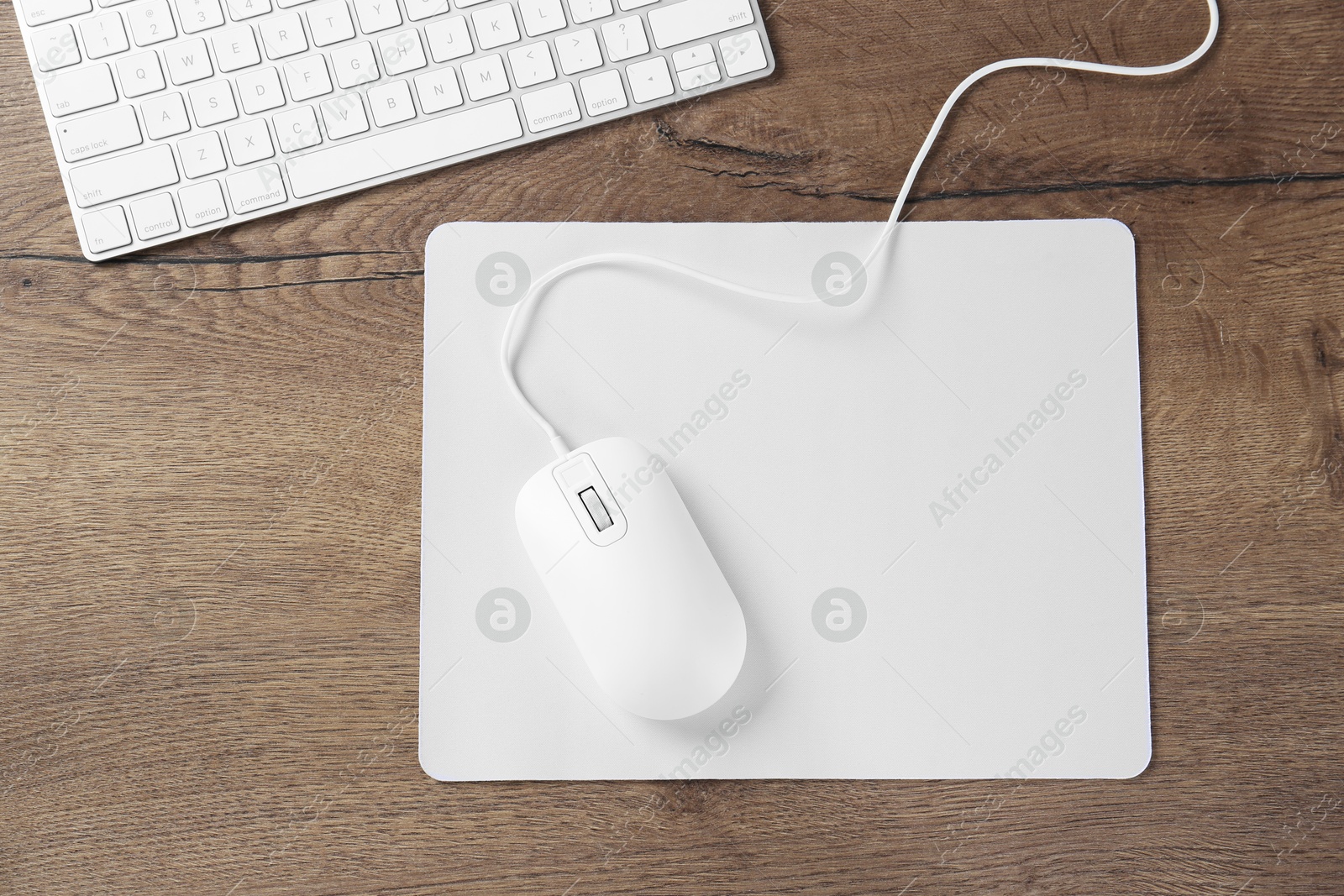 Photo of Computer mouse with mousepad and keyboard on wooden table, flat lay