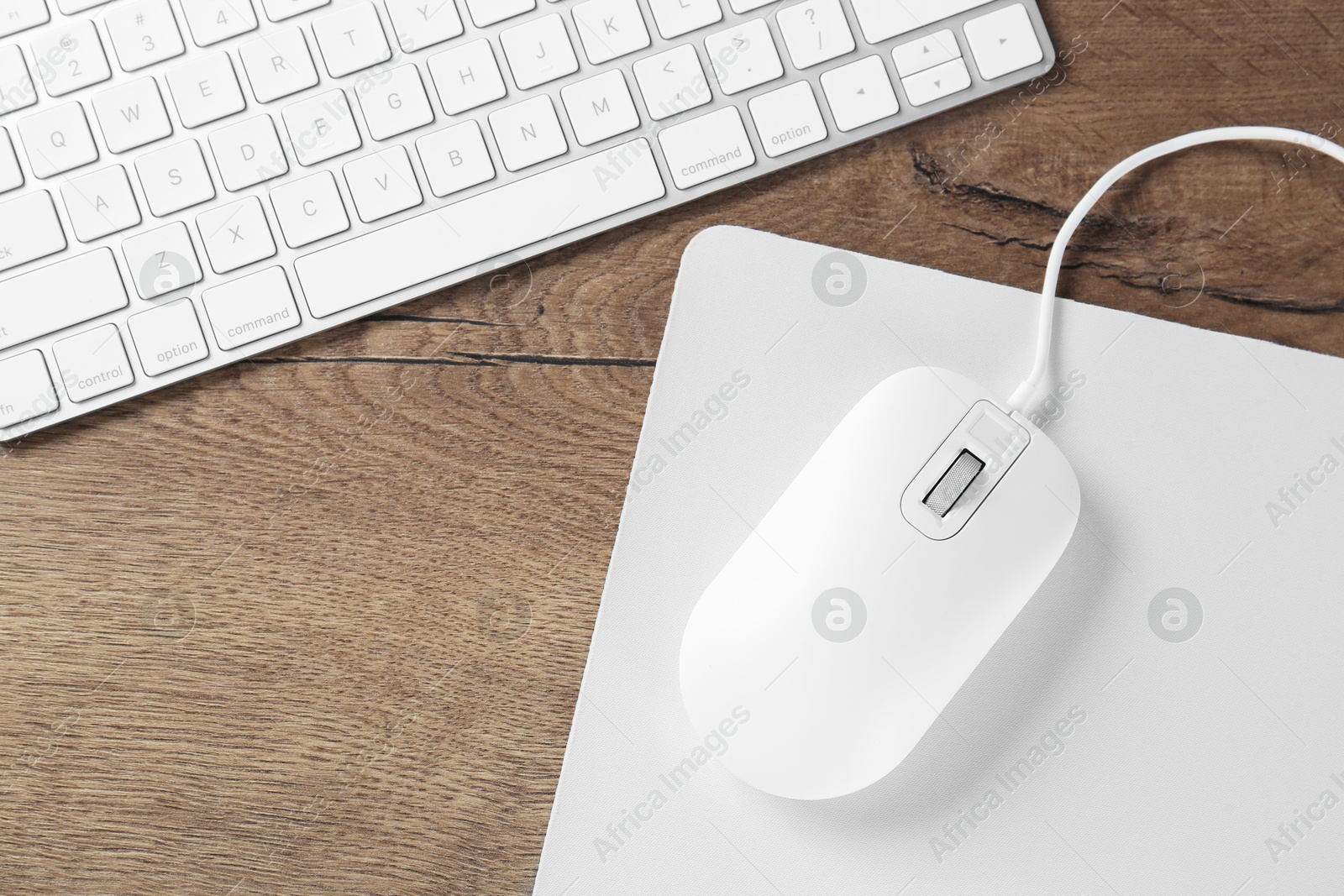 Photo of Computer mouse with mousepad and keyboard on wooden table, flat lay