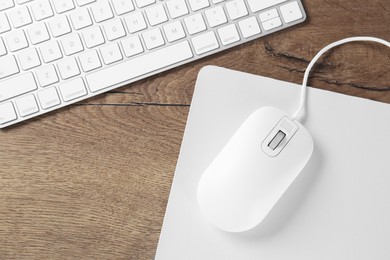 Photo of Computer mouse with mousepad and keyboard on wooden table, flat lay