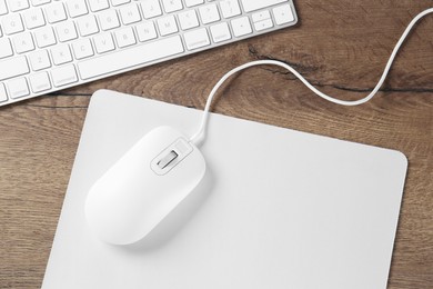 Photo of Computer mouse with mousepad and keyboard on wooden table, flat lay