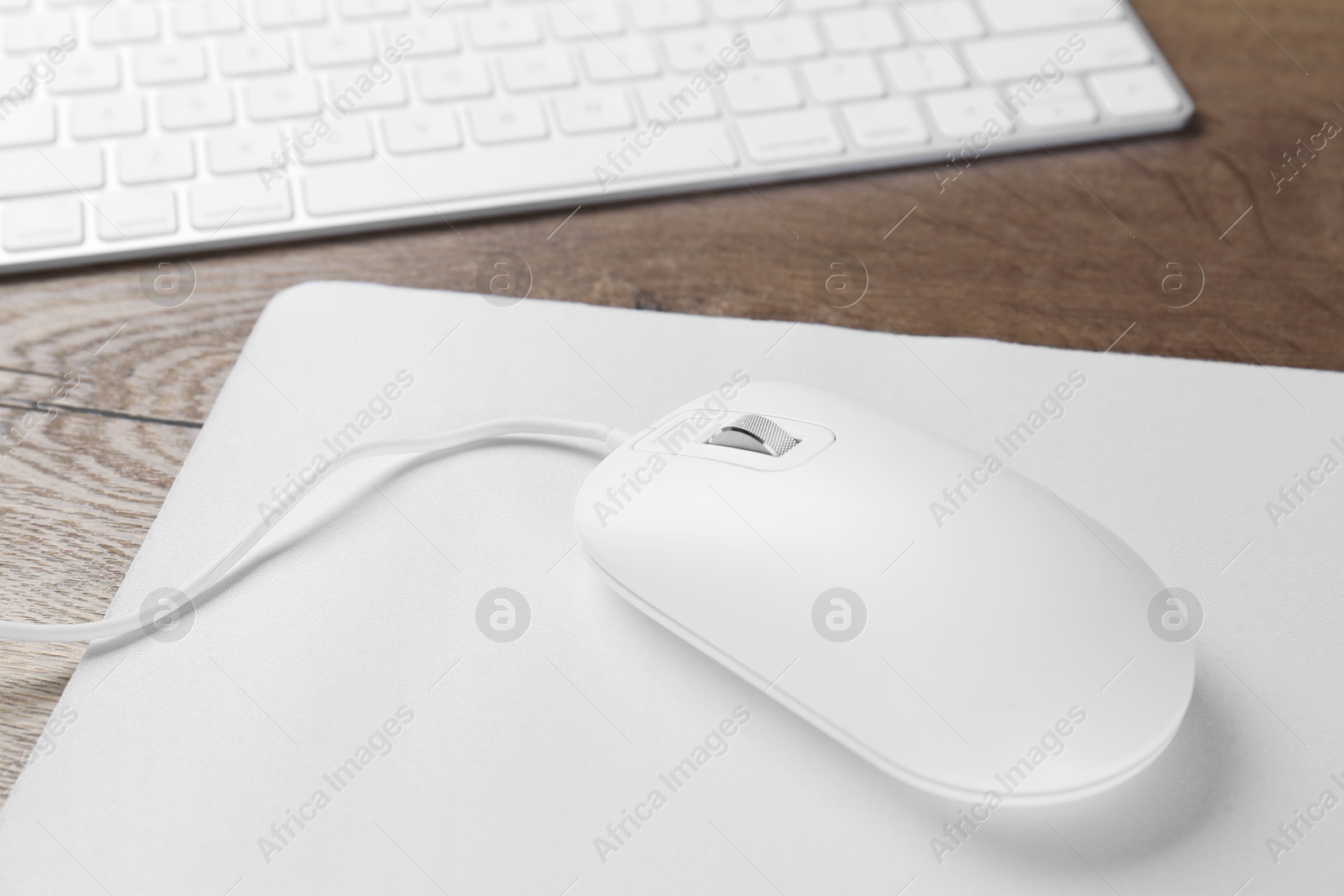 Photo of Computer mouse with mousepad and keyboard on wooden table