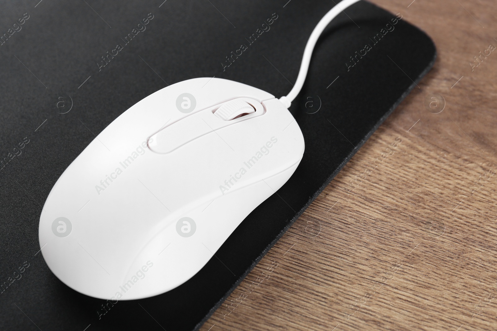 Photo of Computer mouse with mousepad on wooden table, closeup