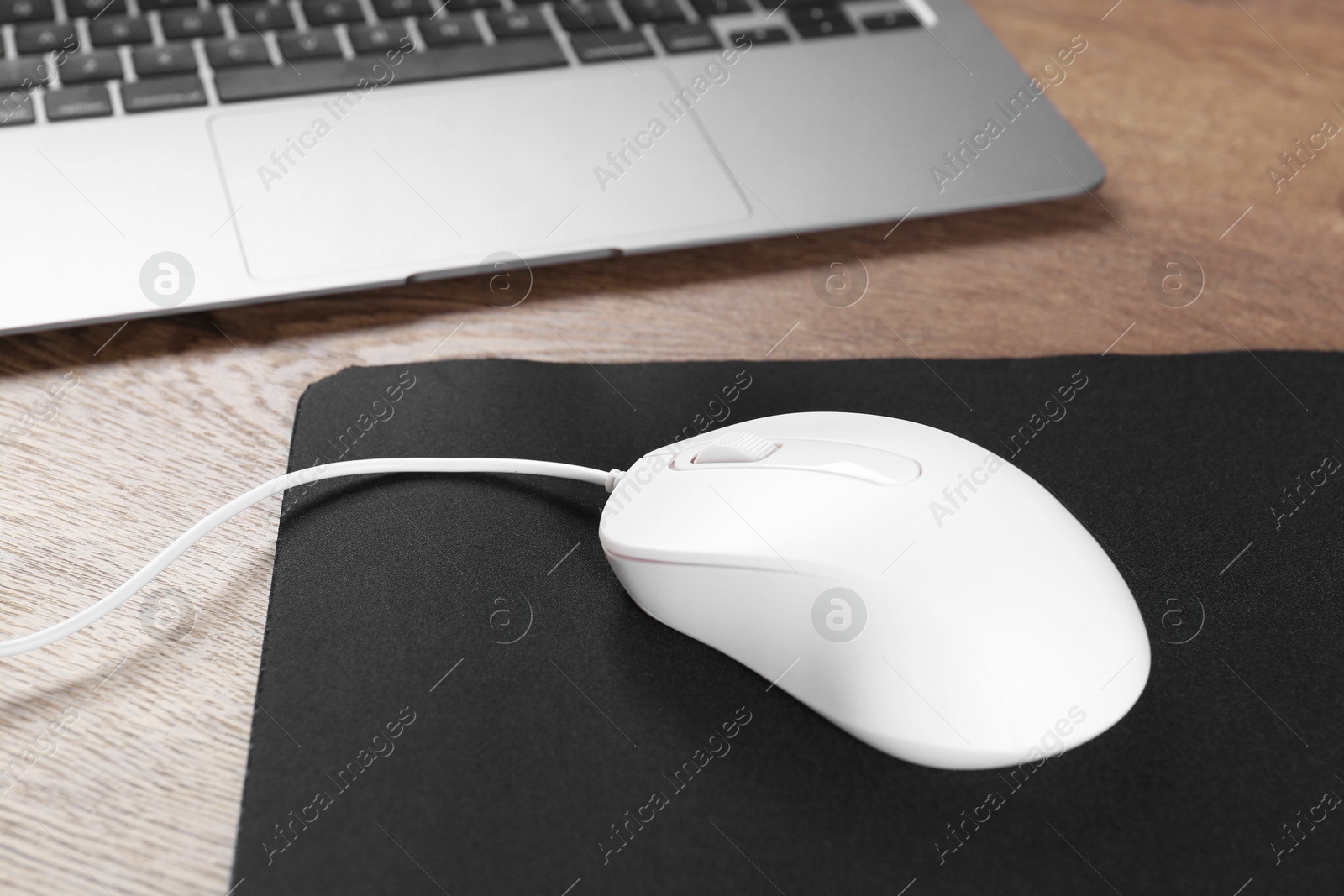 Photo of Computer mouse with mousepad and laptop on wooden table