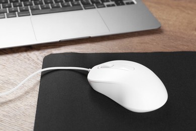 Photo of Computer mouse with mousepad and laptop on wooden table