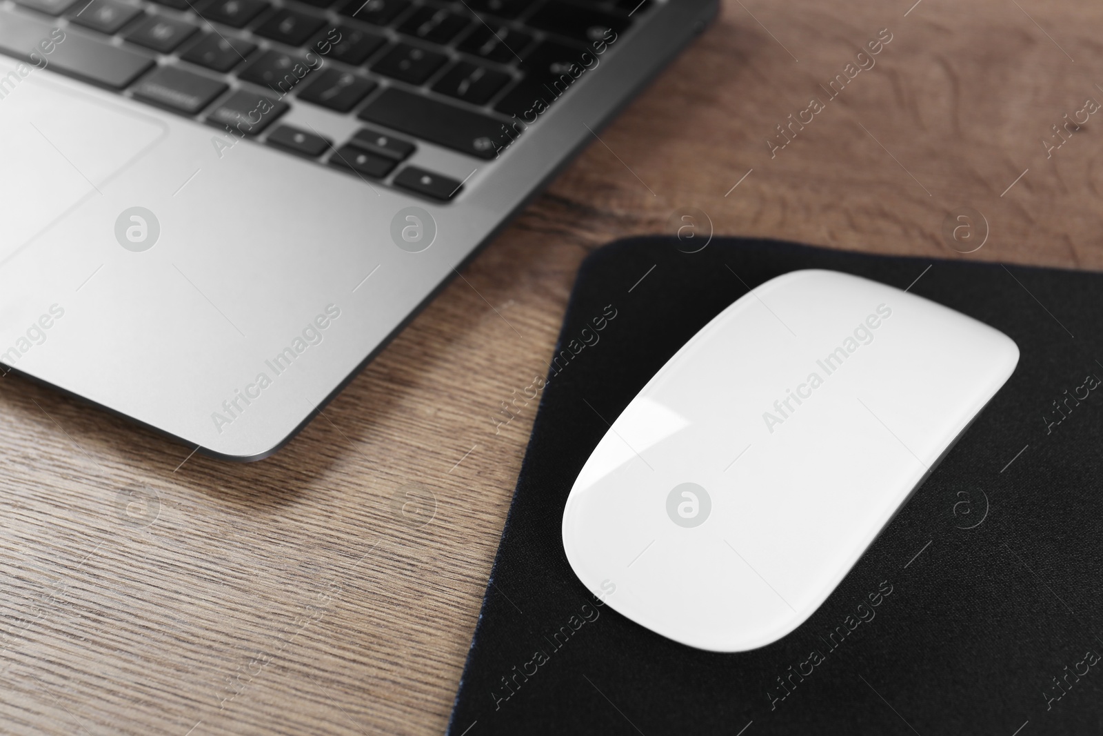 Photo of Computer mouse with mousepad and laptop on wooden table