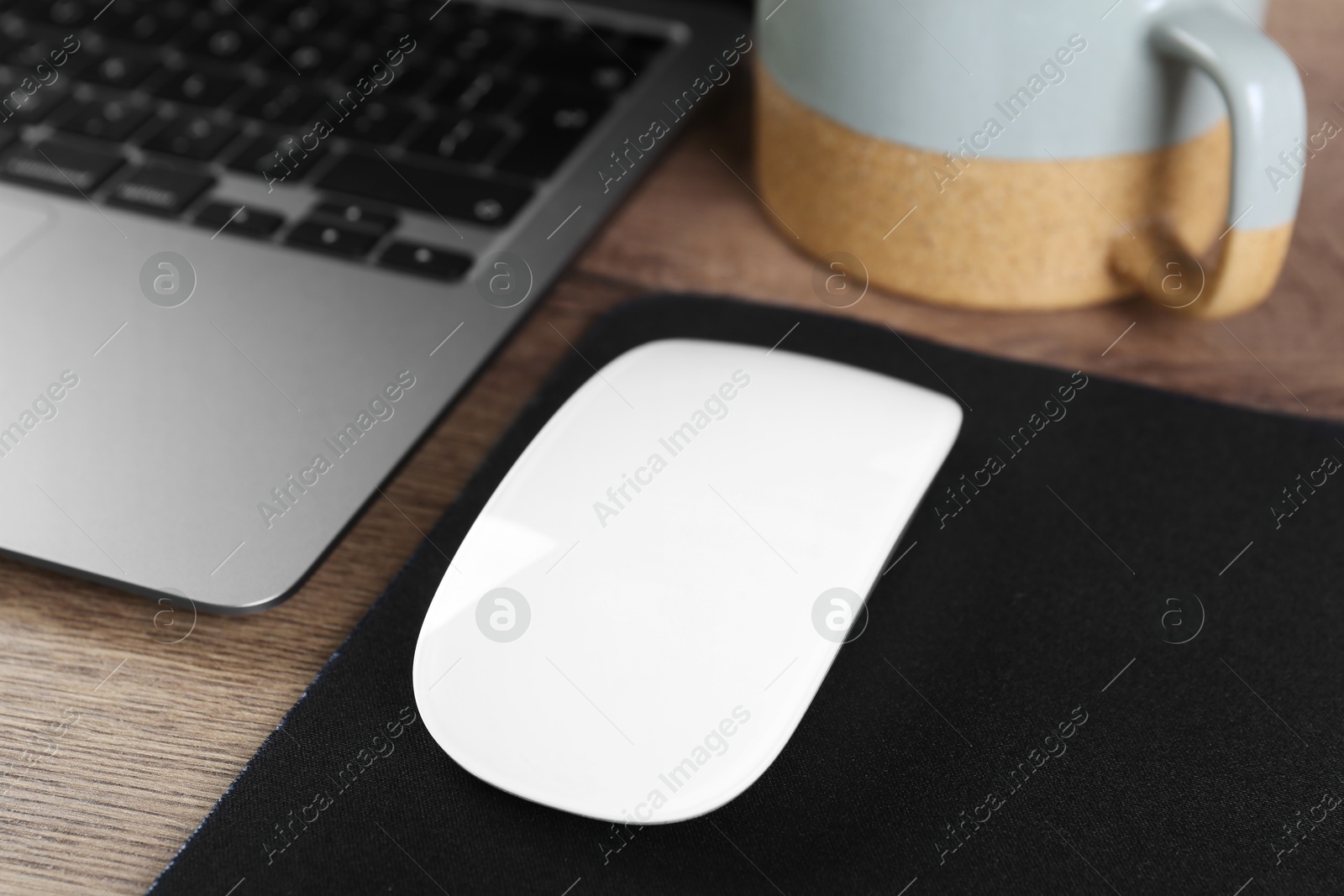 Photo of Computer mouse with mousepad and laptop on wooden table, closeup