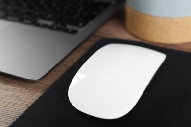 Photo of Computer mouse with mousepad and laptop on wooden table, closeup