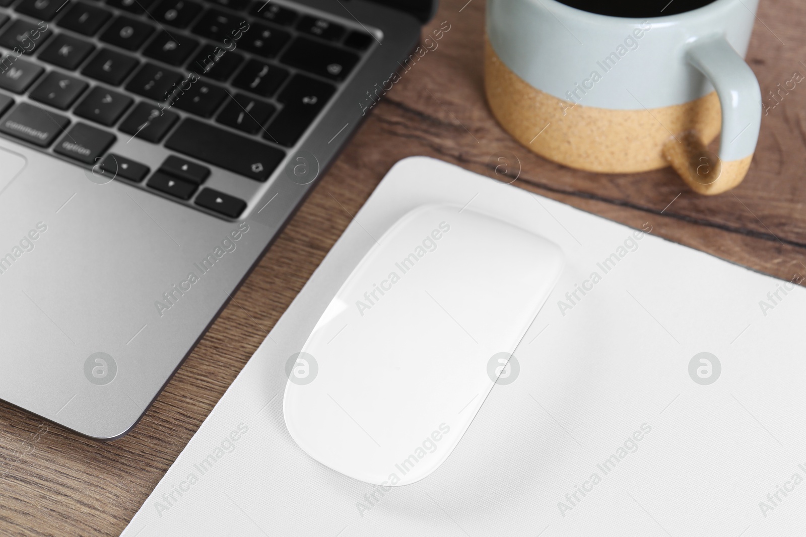 Photo of Computer mouse with mousepad and laptop on wooden table