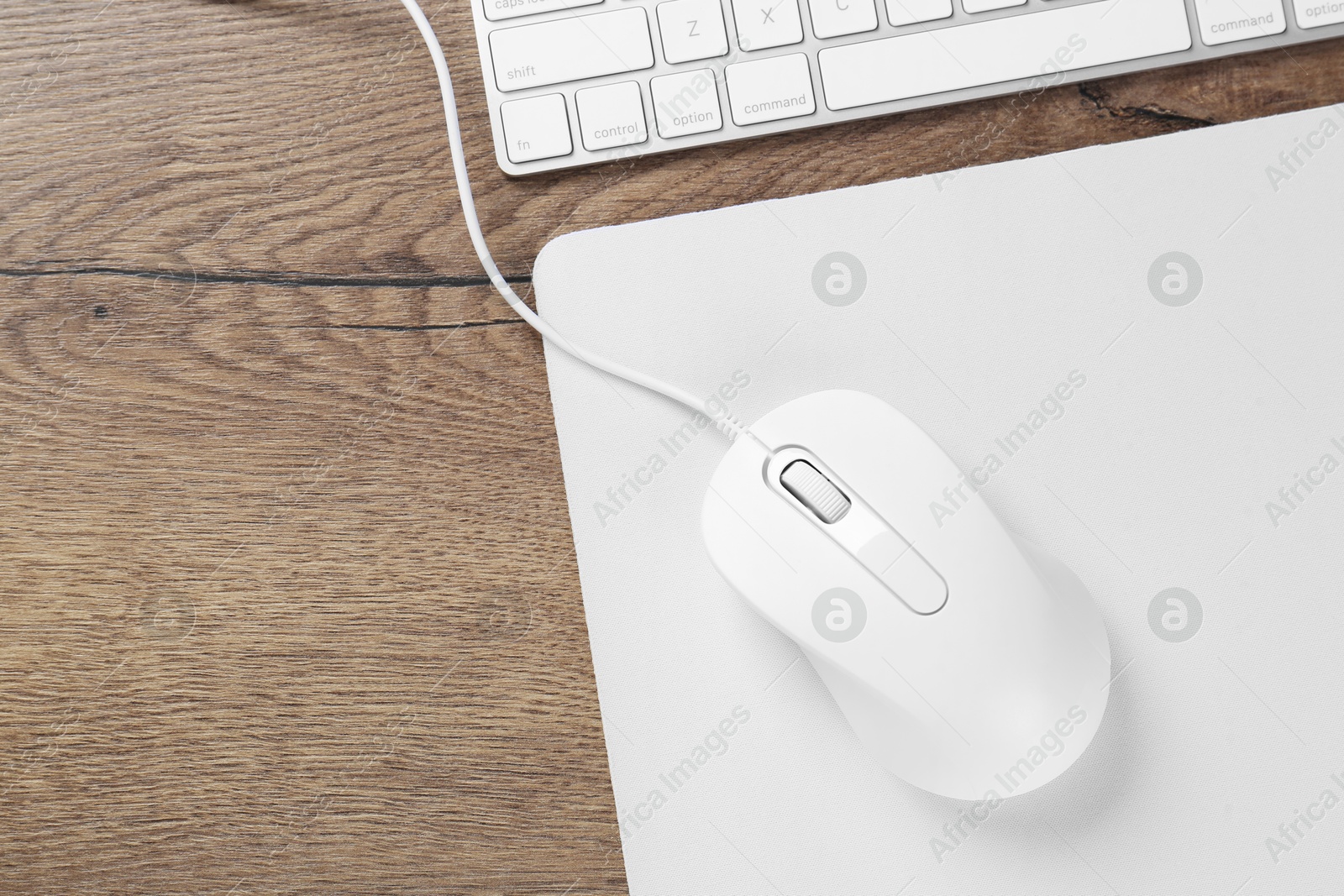 Photo of Computer mouse with mousepad and keyboard on wooden table, flat lay