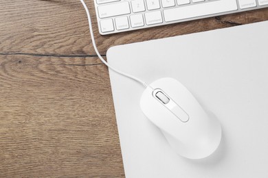 Photo of Computer mouse with mousepad and keyboard on wooden table, flat lay