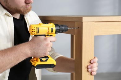 Photo of Man with electric screwdriver assembling table indoors, closeup