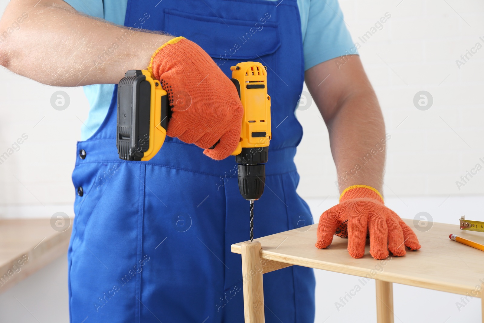 Photo of Worker with electric screwdriver assembling furniture indoors, closeup