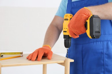 Photo of Worker with electric screwdriver assembling furniture indoors, closeup