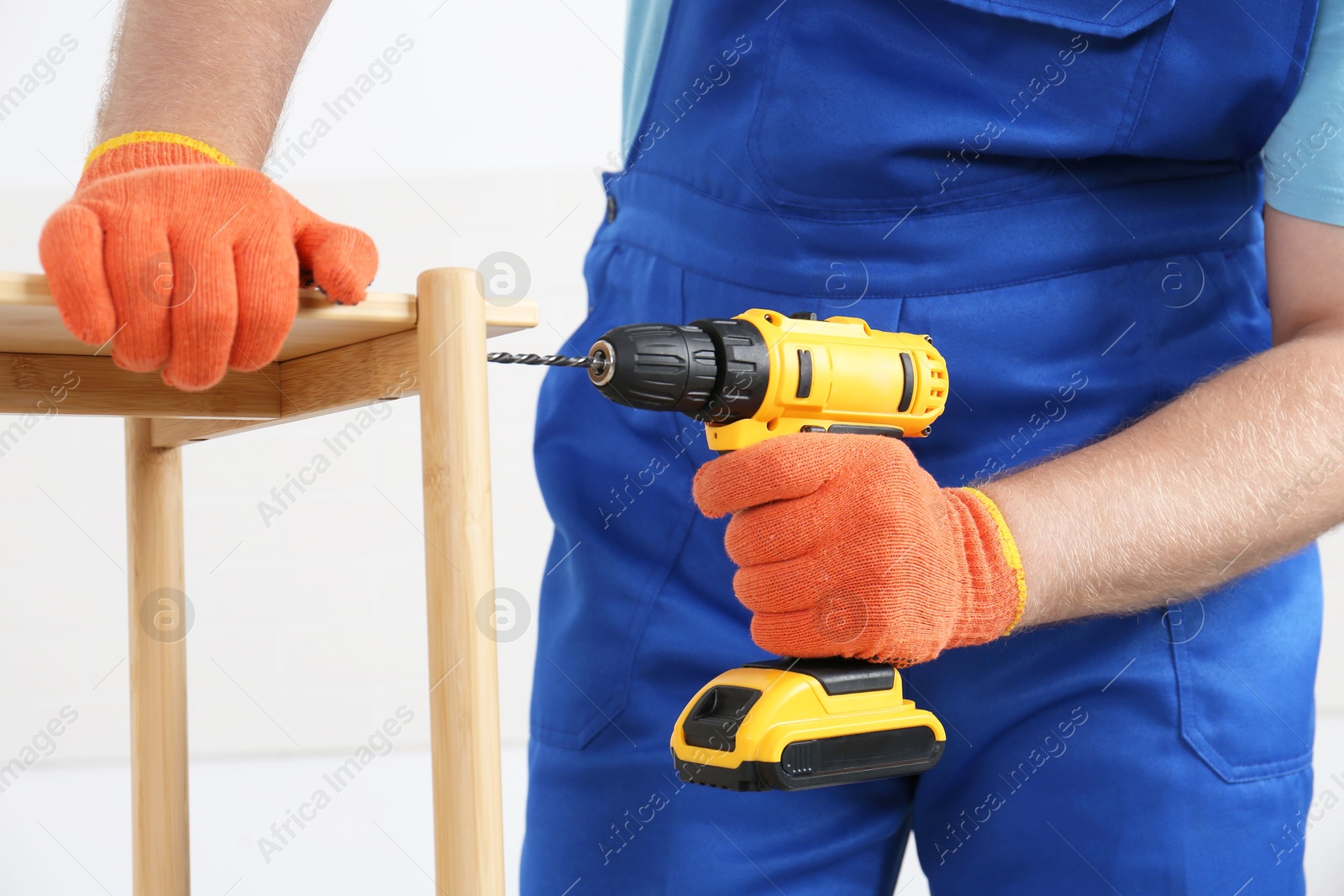 Photo of Worker with electric screwdriver assembling furniture indoors, closeup