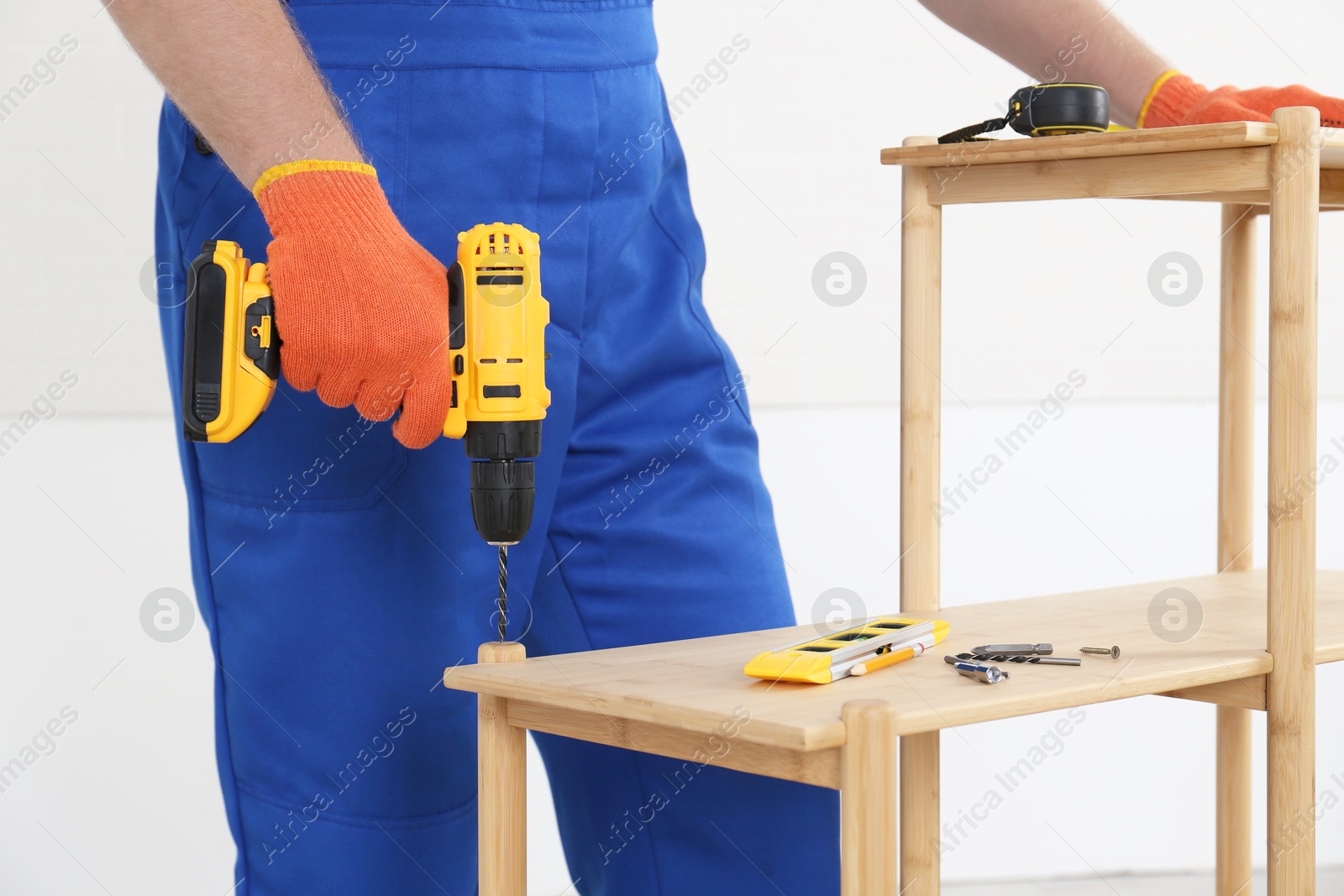 Photo of Worker with electric screwdriver assembling furniture indoors, closeup