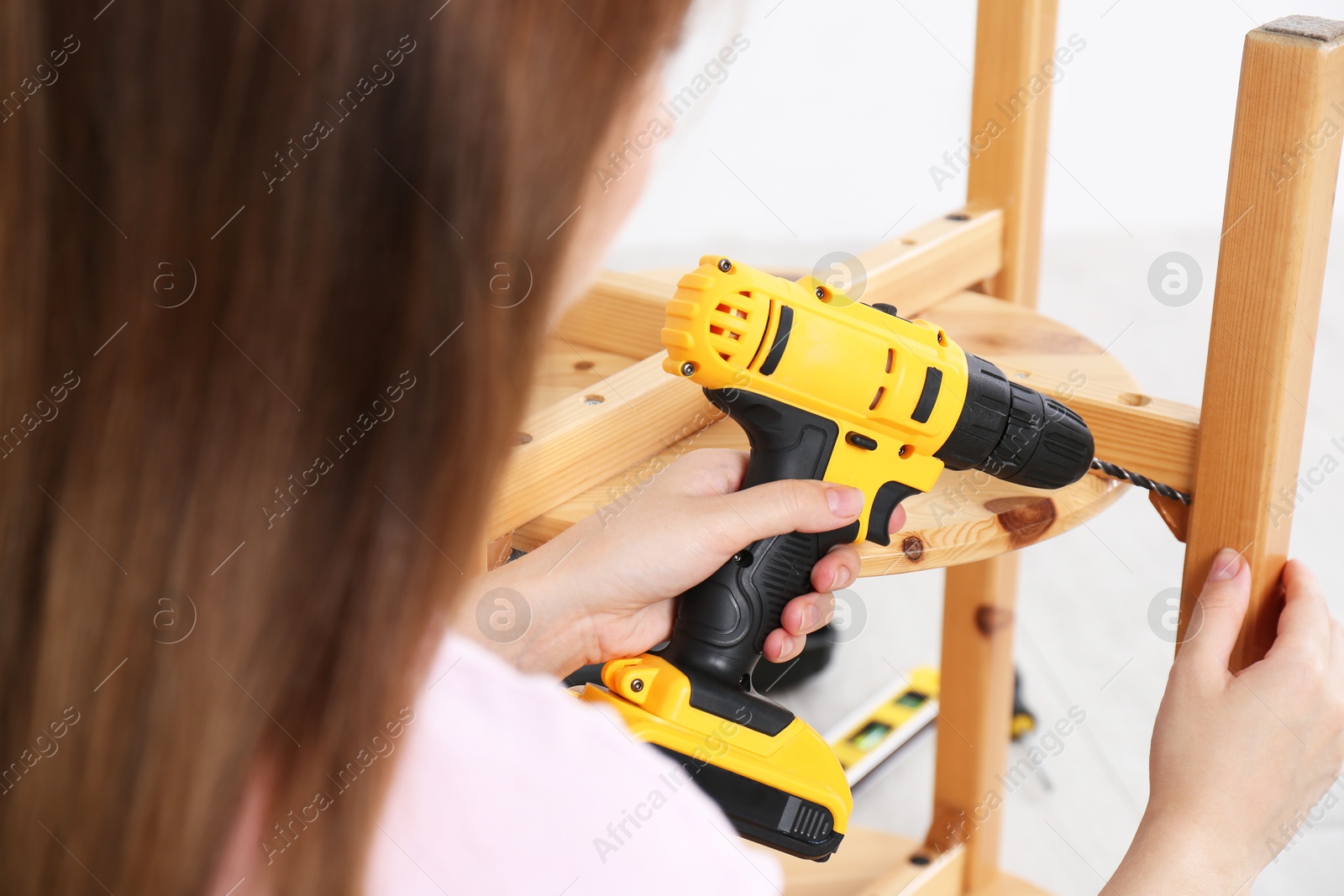 Photo of Woman with electric screwdriver assembling furniture indoors, closeup