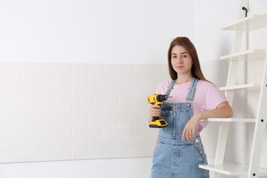 Photo of Woman with electric screwdriver indoors. Assembling furniture. Space for text