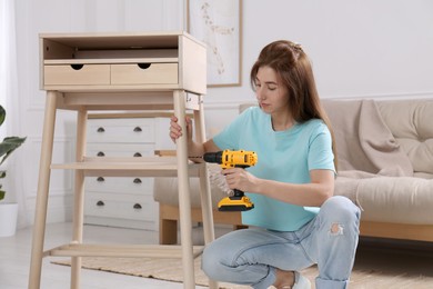 Photo of Woman with electric screwdriver assembling table in room