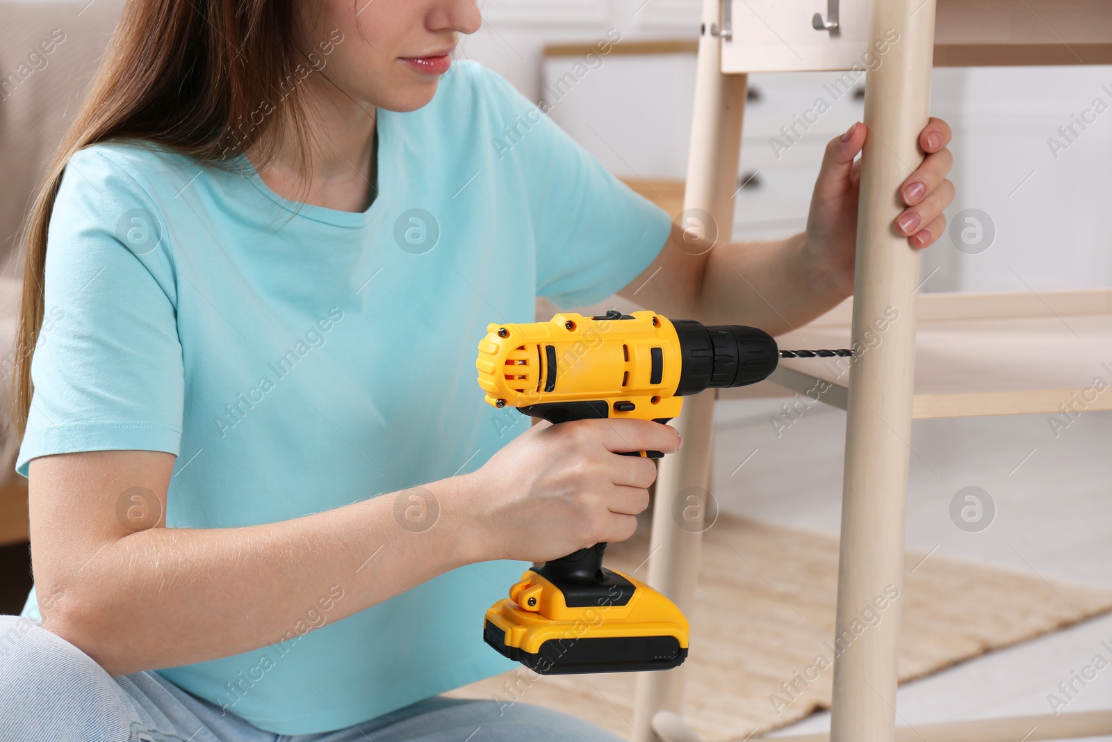 Photo of Woman with electric screwdriver assembling furniture in room, closeup