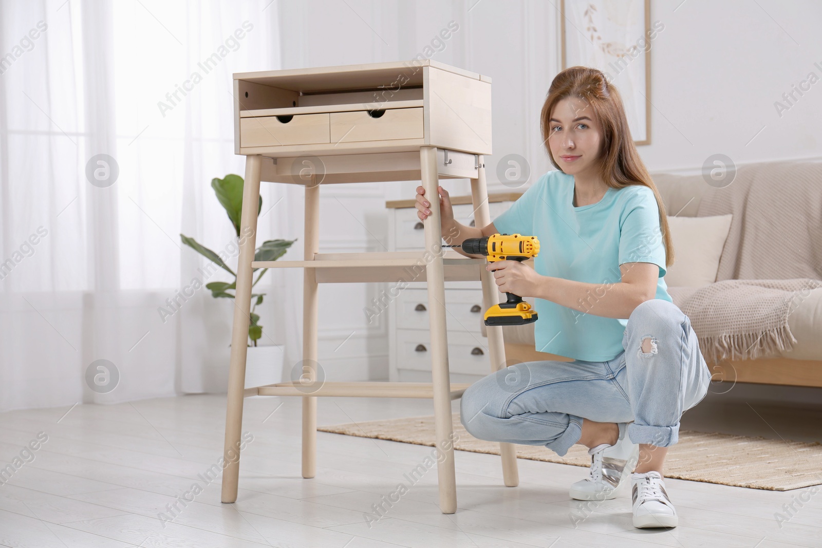 Photo of Woman with electric screwdriver assembling table in room