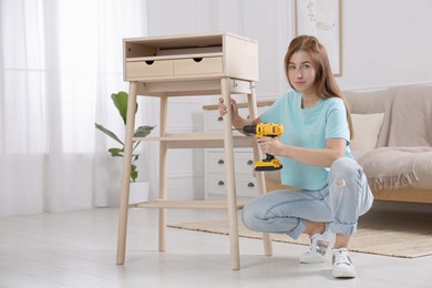 Woman with electric screwdriver assembling table in room