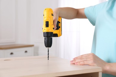 Photo of Woman with electric screwdriver assembling furniture at home, closeup