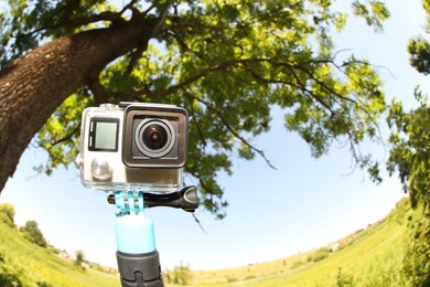 Photo of Modern action camera with monopod outdoors, space for text. Fisheye lens effect