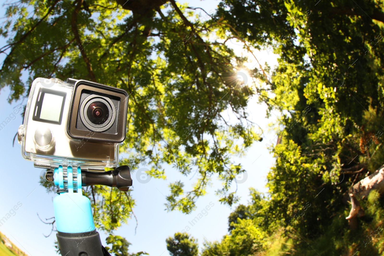 Photo of Modern action camera with monopod outdoors, space for text. Fisheye lens effect