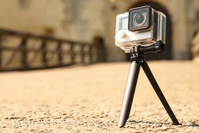 Modern action camera with tripod outdoors. Space for text