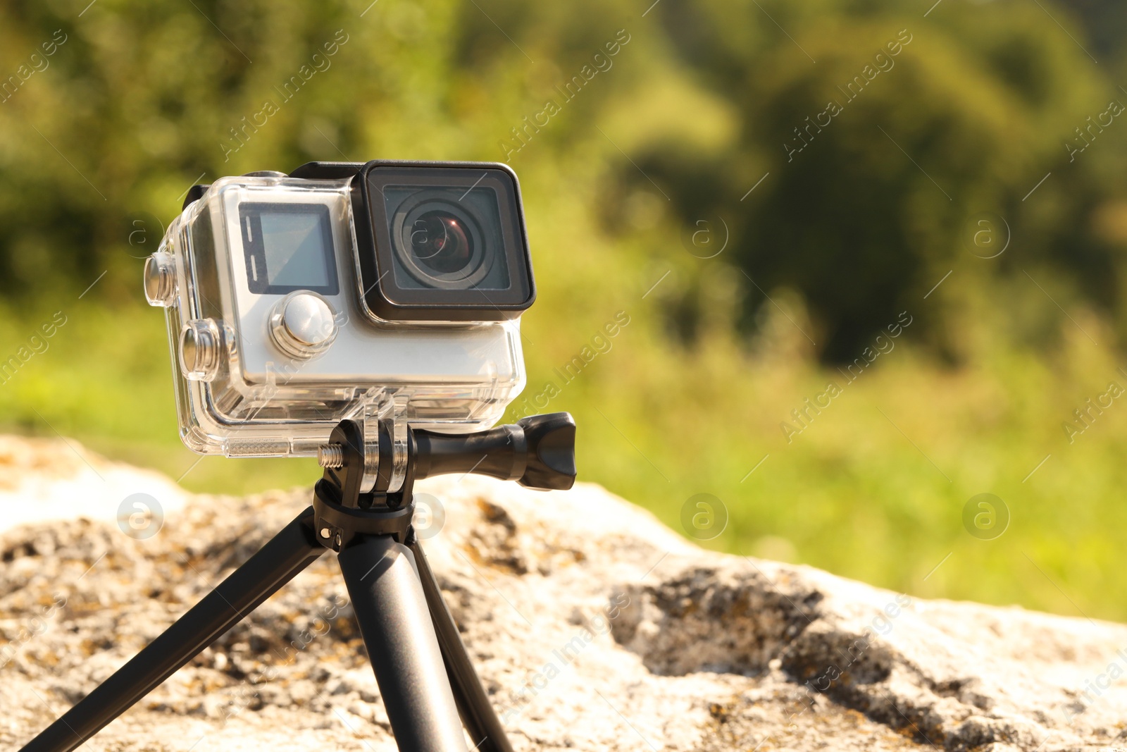 Photo of Modern action camera with tripod on stone outdoors, space for text