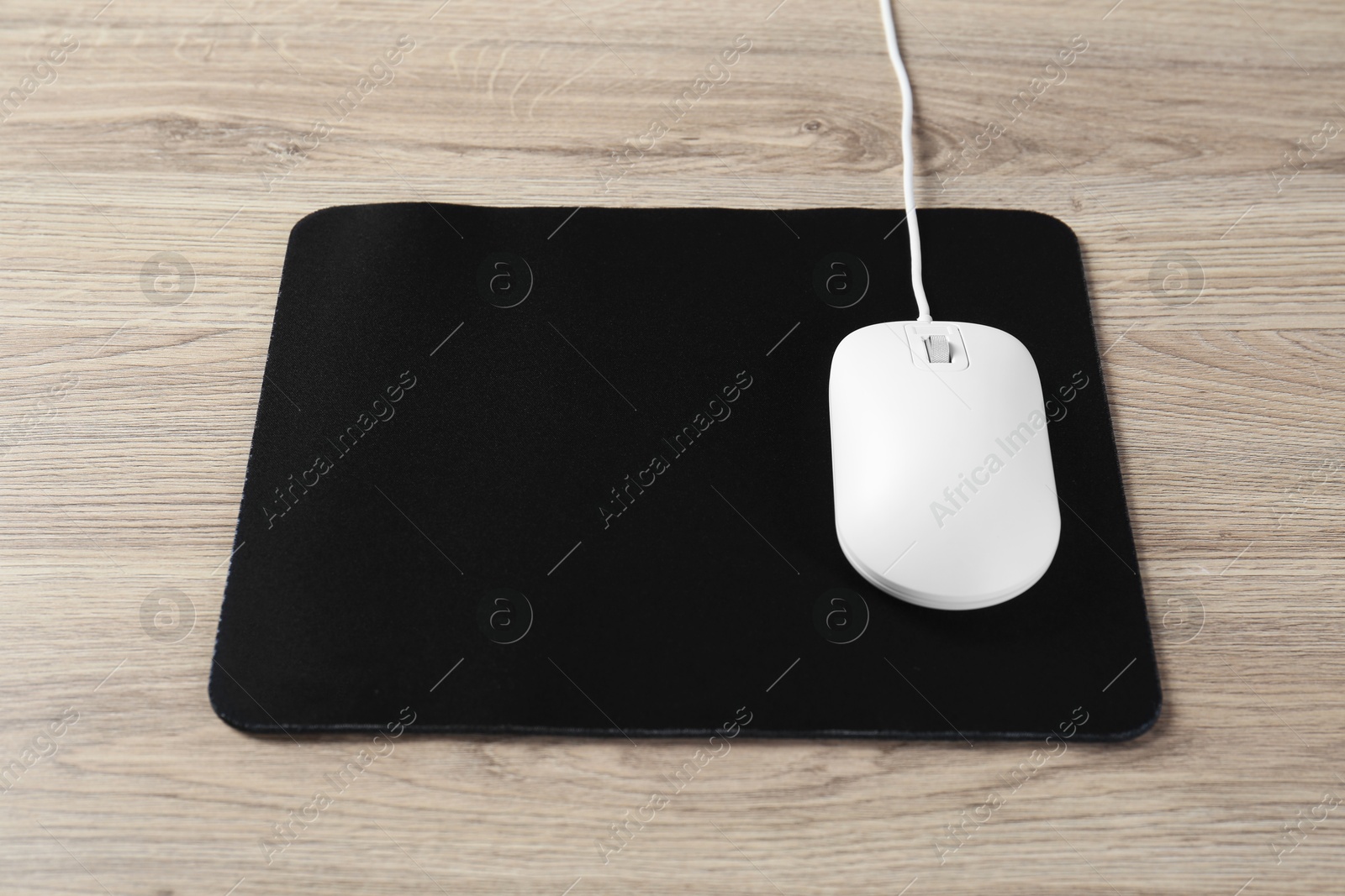 Photo of White computer mouse and black mousepad on wooden table