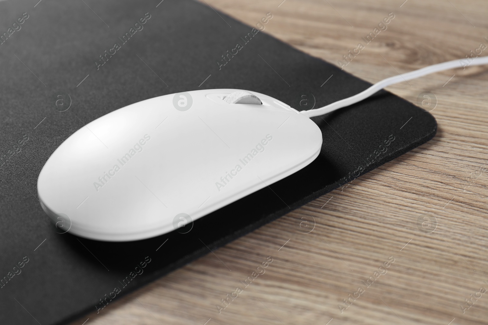 Photo of White computer mouse and black mousepad on wooden table, closeup