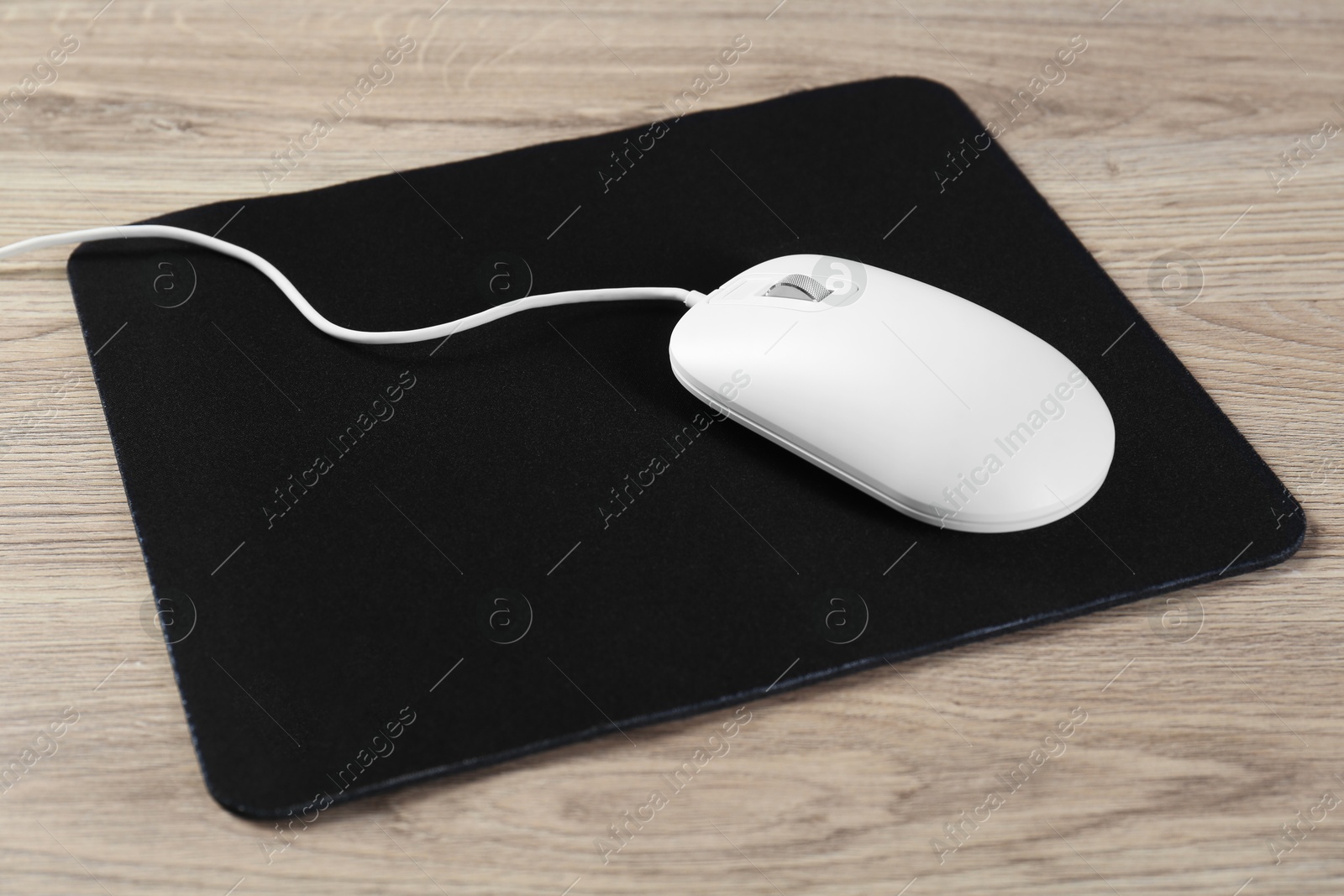 Photo of White computer mouse and black mousepad on wooden table, closeup