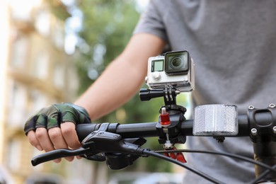 Photo of Man riding bicycle with modern action camera outdoors, closeup