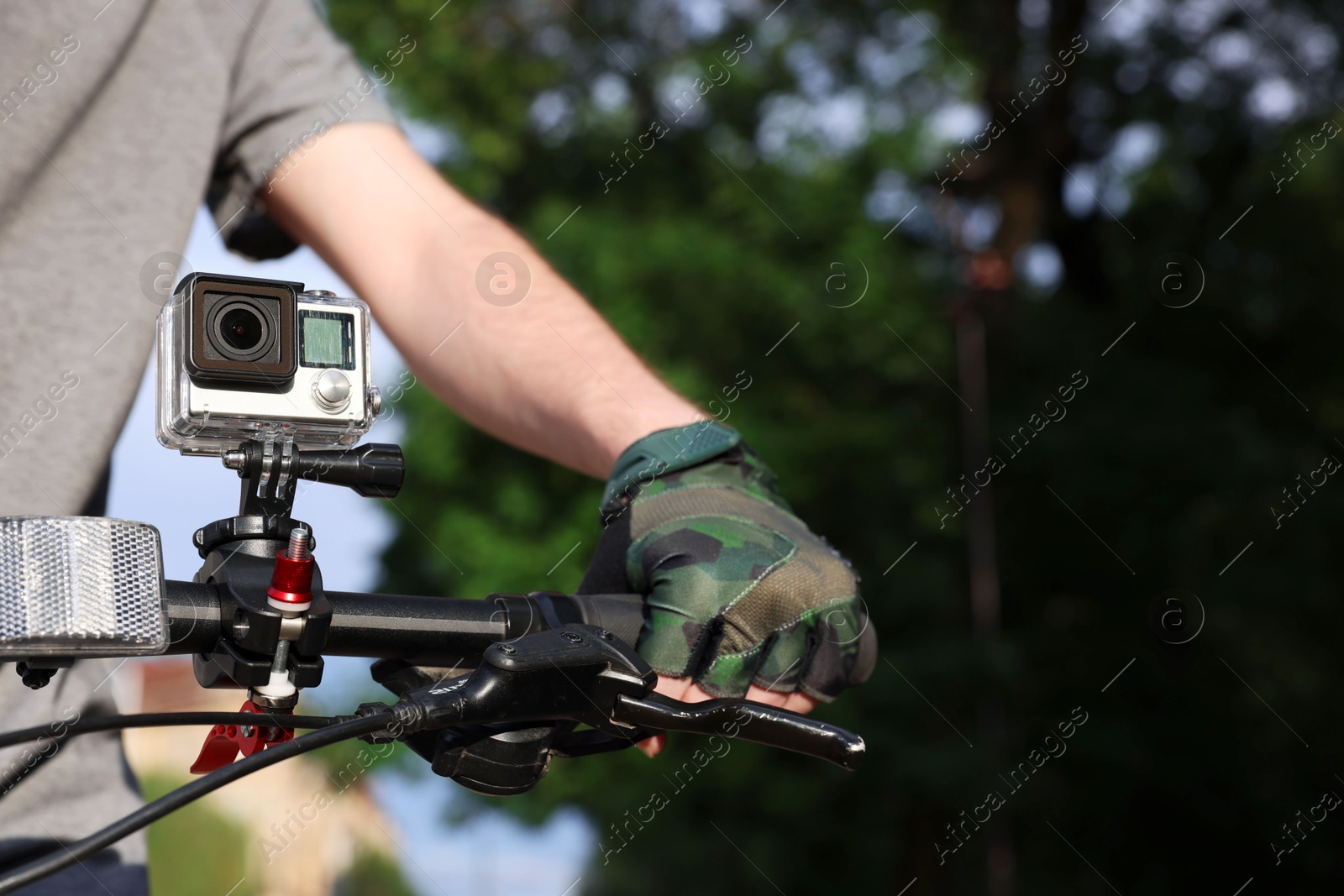 Photo of Man riding bicycle with modern action camera outdoors, closeup