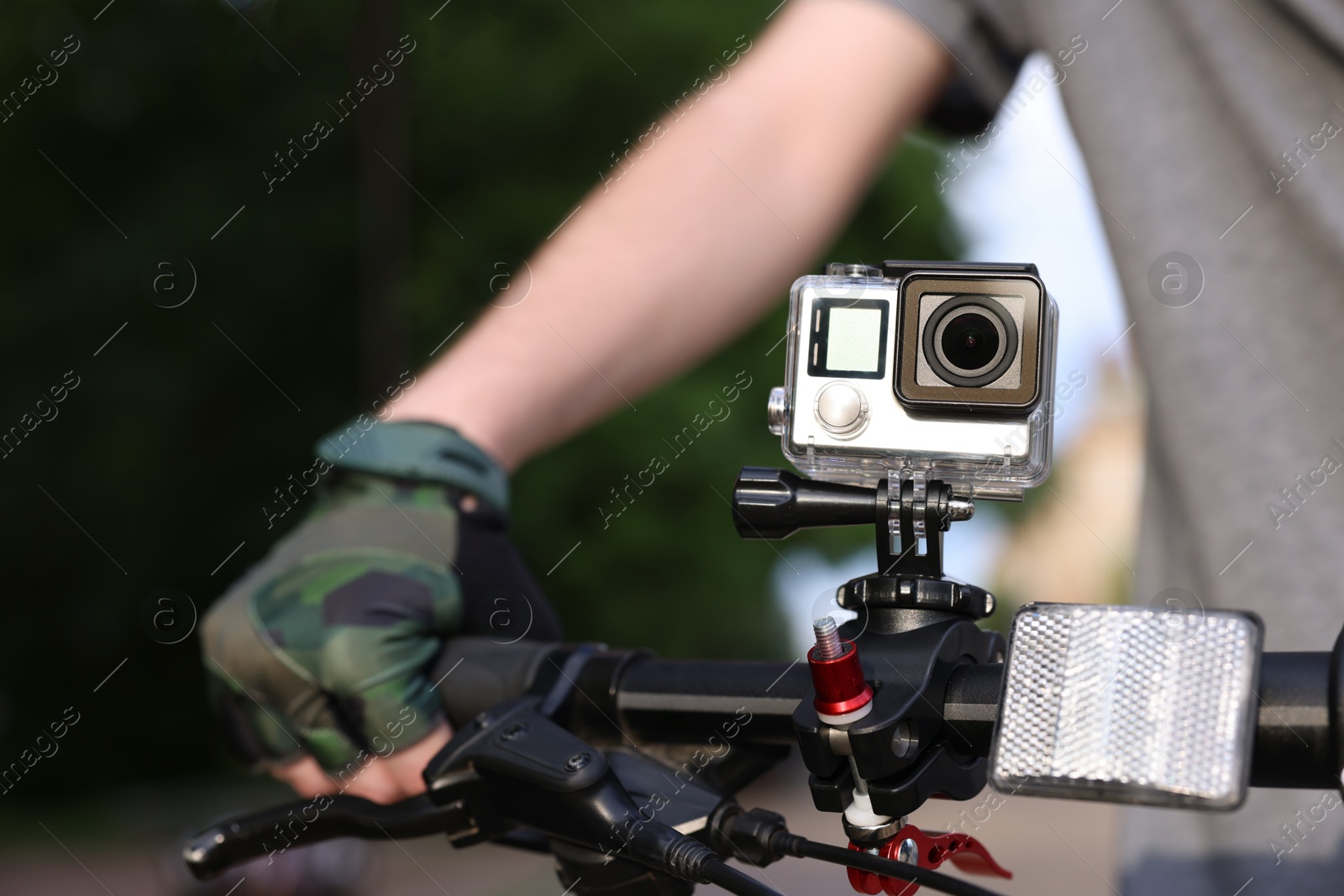 Photo of Man riding bicycle with modern action camera outdoors, closeup